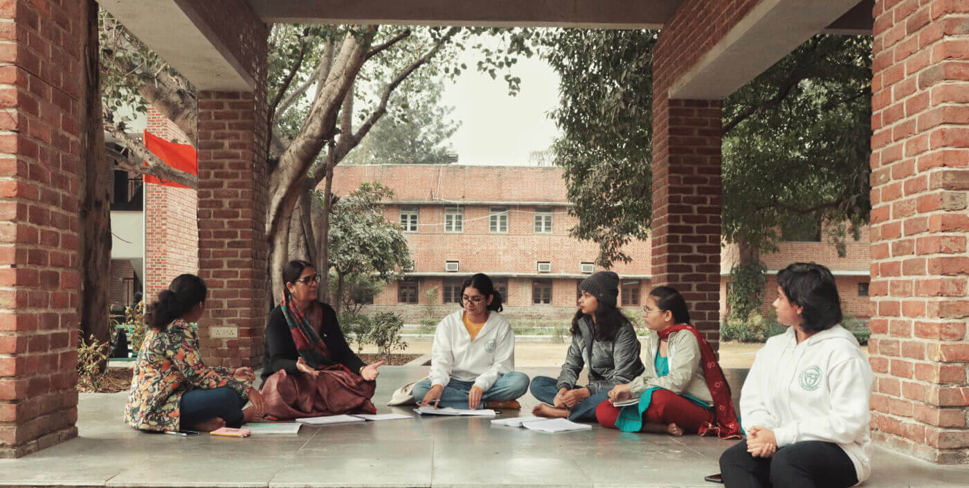 Students and a teacher in discussion under the red-brick colonnade, with a heritage residential block behind